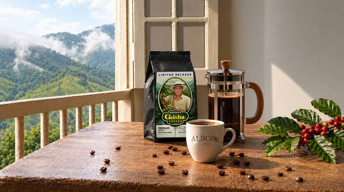 Un sachet de café Gustavo’s Geisha, une cafetière à piston et une tasse ALBOR fumante sur une table en bois, près d’un balcon donnant sur des montagnes couvertes de caféiers dans la brume